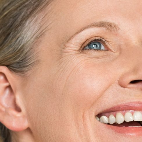 Portrait of a cheerful senior woman smiling while looking away isolated on gray background. Happy mature woman after spa massage and anti-aging treatment on face.